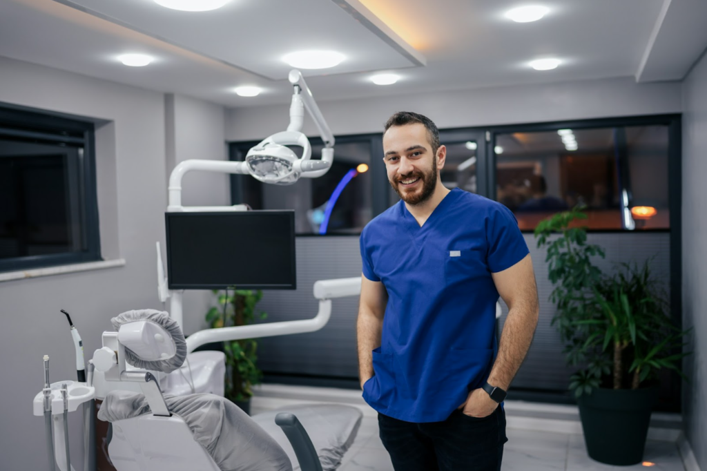 A male dental assistant with his hands in his pockets smiling in the surgery room